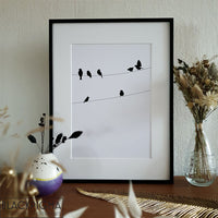 Encadrement de l'affiche minimaliste en noir et blanc représentant des petits oiseaux sur un fil.